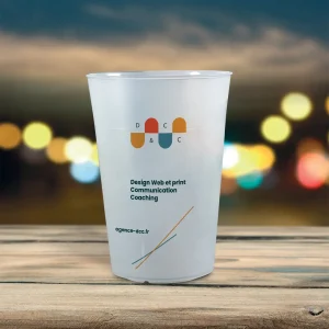 Un gobelet en plastique avec un design imprimé et du texte, placé sur une surface en bois contre un arrière-plan flou de lumières, mettant en valeur le branding du gobelet.