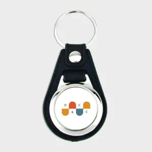 Porte-clés personnalisé avec le logo d’une entreprise, attaché à un anneau métallique et une sangle en cuir noir, illustrant un article sur la préparation d’un salon professionnel.